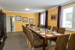 Uma sala de jantar com uma mesa comprida posta para seis pessoas, cadeiras e um armário.