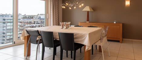 A modern dining area with a table set for four, a wooden sideboard, and a city view through large windows.