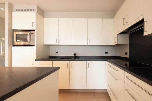 Una cocina moderna con armarios blancos, horno integrado y encimera negra.