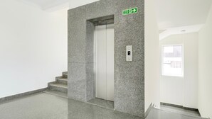 Ein moderner, sauberer Aufzug mit einem Feuerausgangsschild, einer Treppenhausöffnung und einer Tür mit Fenster.
