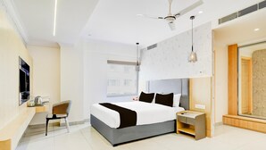 Ein modernes Hotelzimmer mit einem großen Bett, einem Schreibtisch, einem Sessel, einem Nachttisch, einem Deckenventilator und einem großen Spiegel.