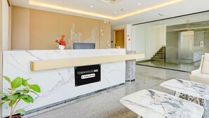 Ein Hotel-Empfangsbereich mit einem Marmor-Empfangstresen, einer Pflanze und einer Treppe im Hintergrund.