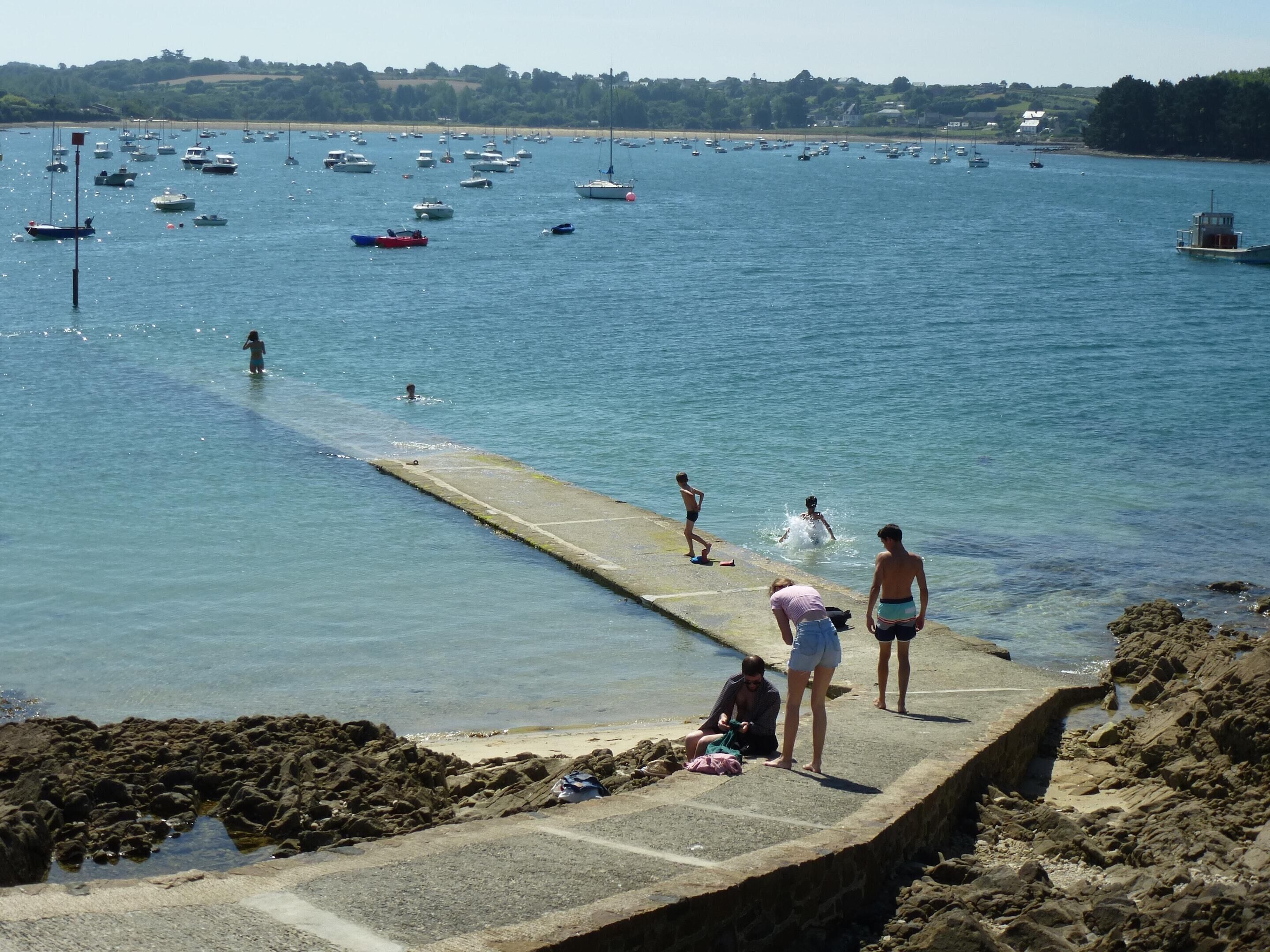 A coastal scene with a pier extending into calm waters, surrounded by boats and a distant shoreline.