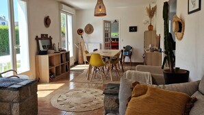 A living room with a stone fireplace, a dining area with a wooden table and chairs, and a large window with a view of greenery. - Family Home in Locquirec Bay (Locquirec)