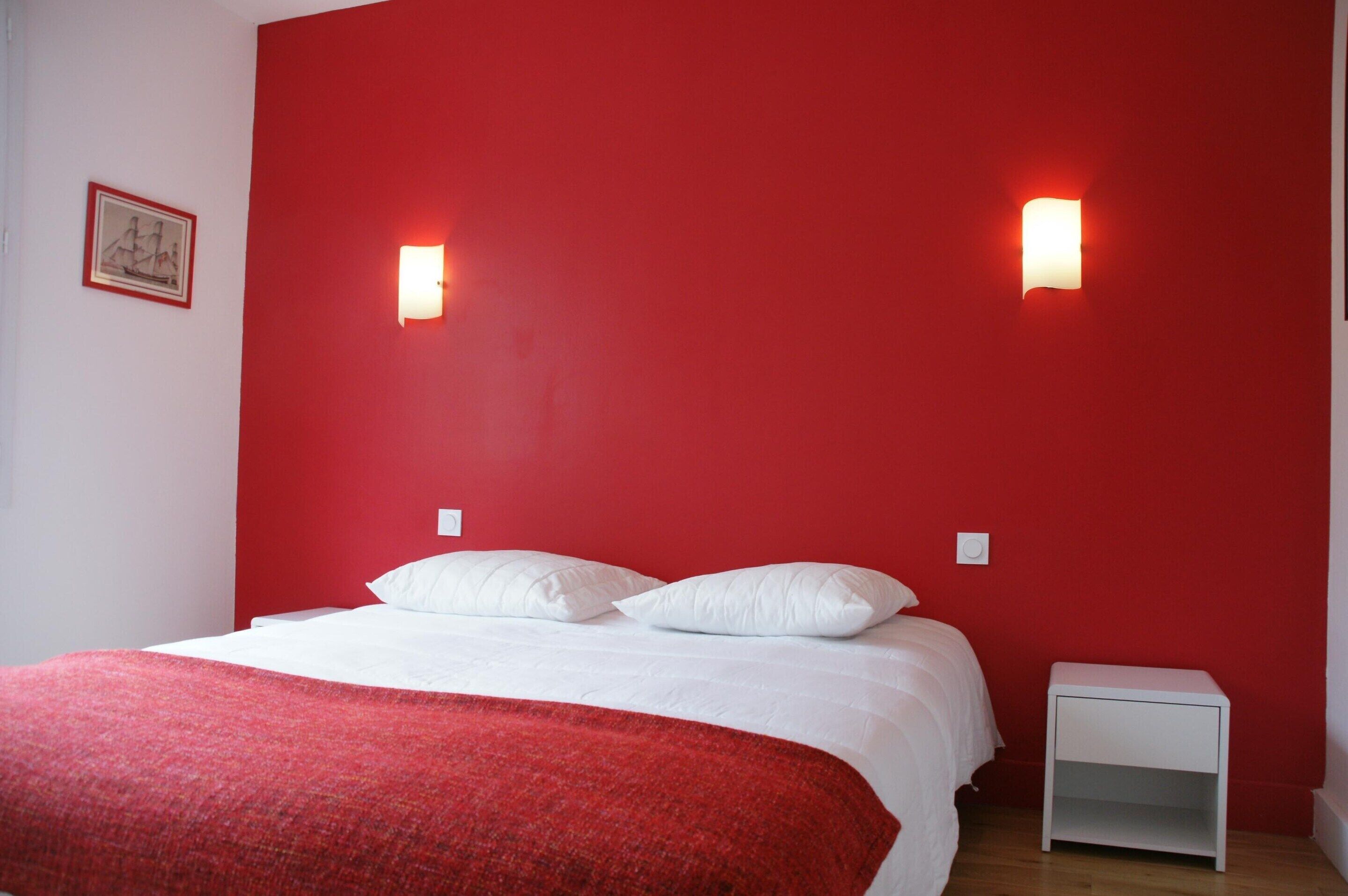 Een kamer met een bed, een rode muur en twee wandlampen.