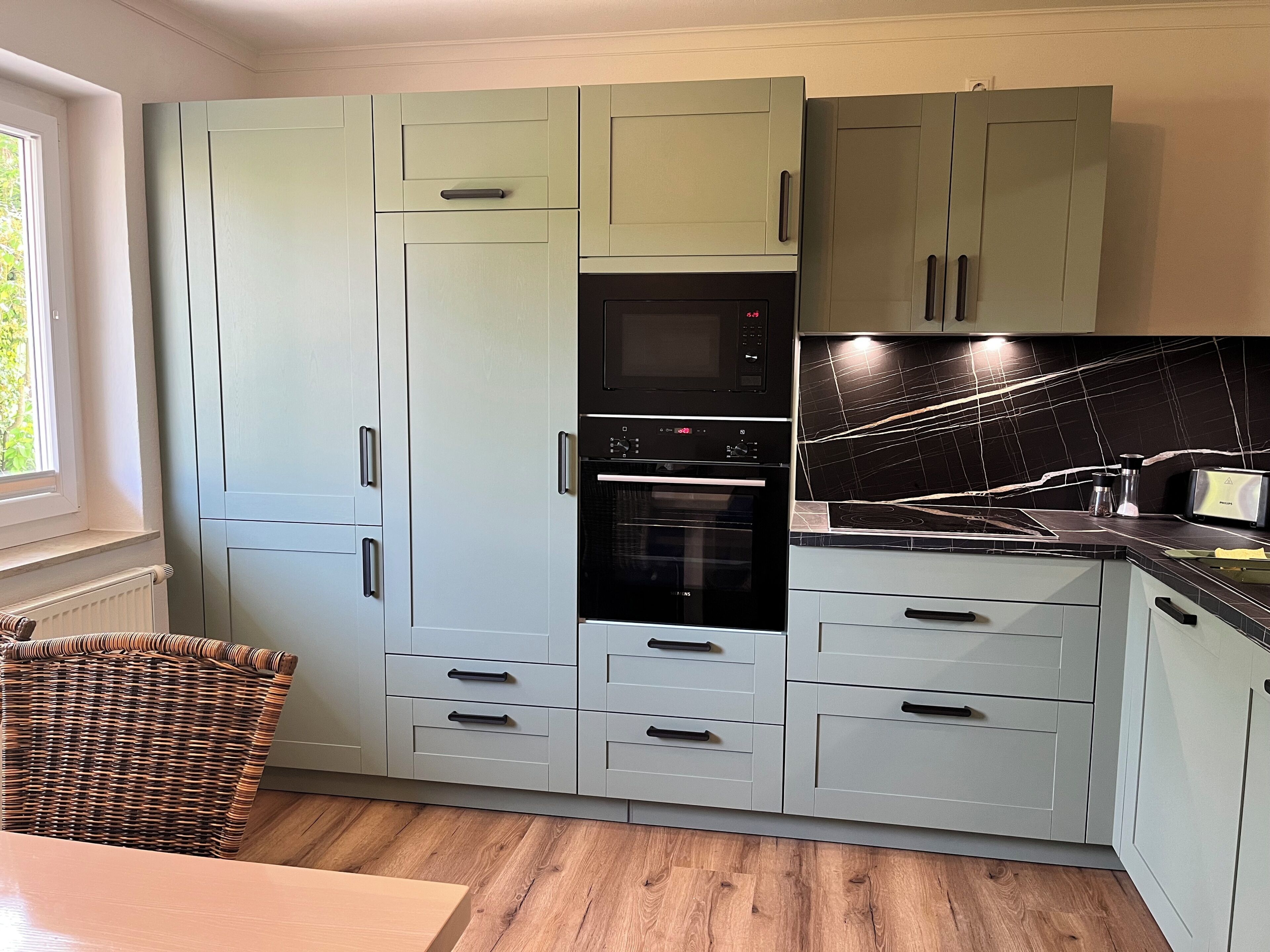 Keittiössä on vaaleansiniset kaapit, musta uuni ja musta mikroaaltouuni.