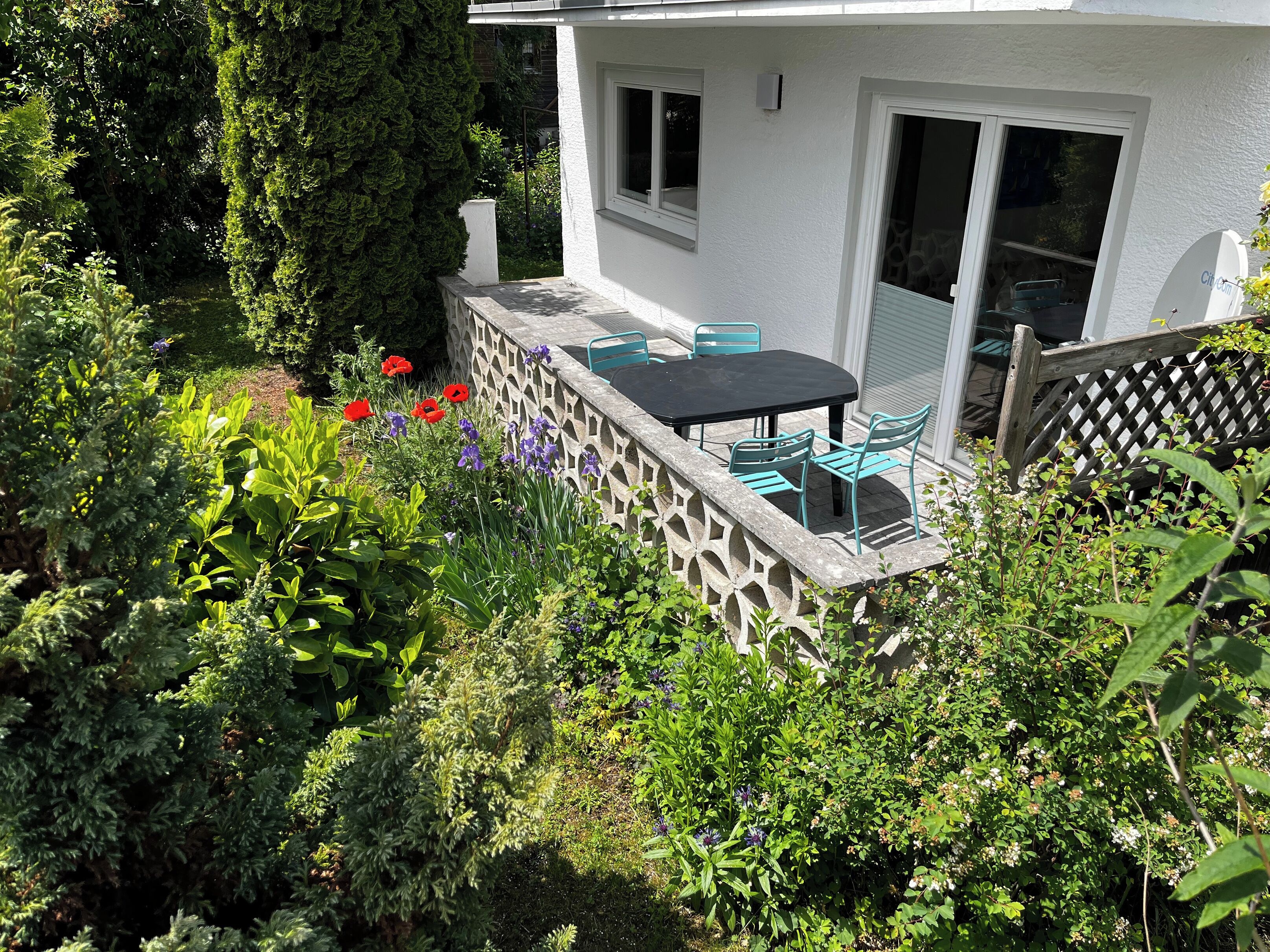 Una casa con patio, un recinto bianco e un giardino pieno di piante e fiori.