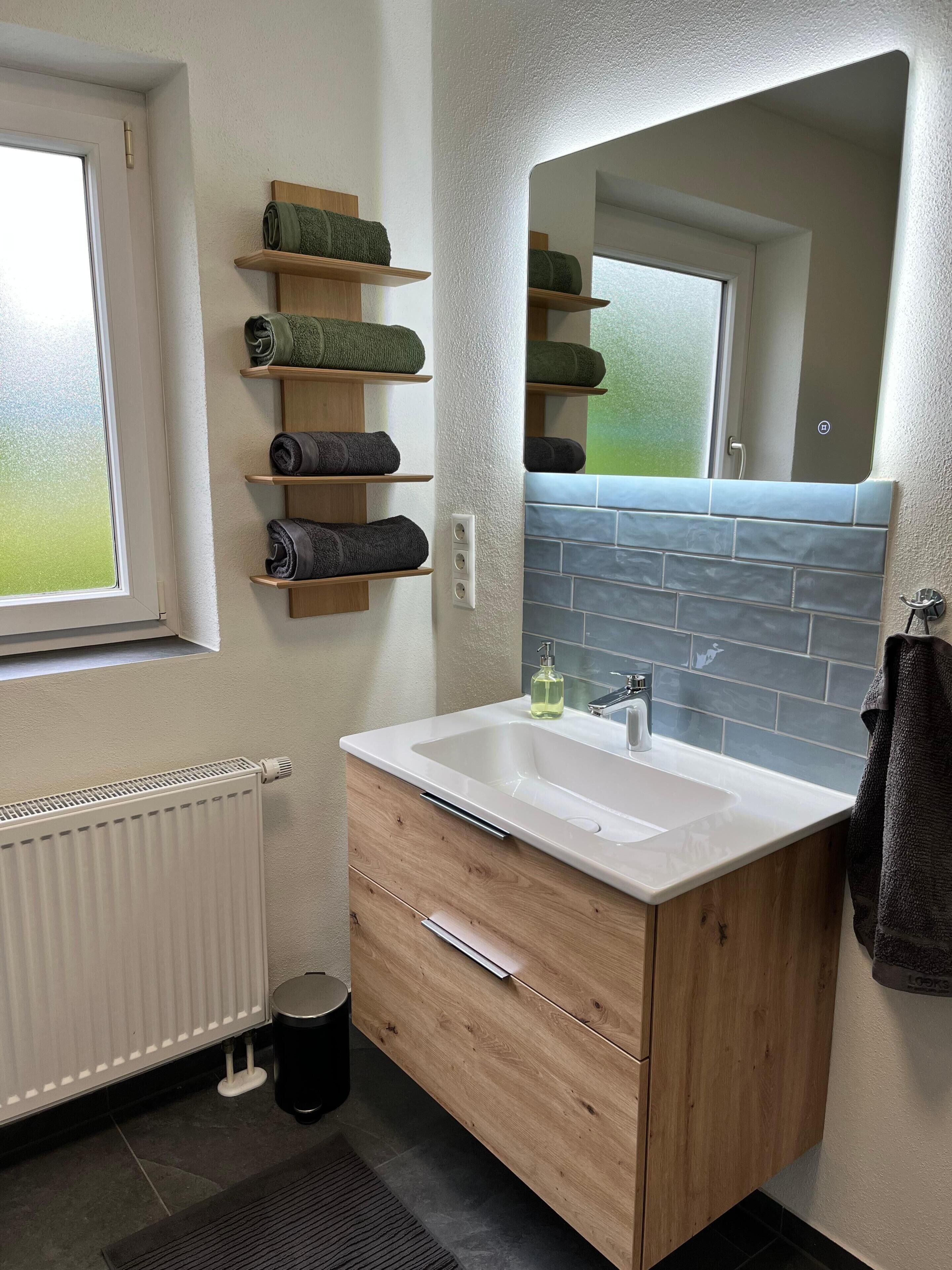 A bathroom with a white sink, wooden vanity, towel racks, a mirror, and a window.