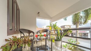 A balcony with a glass table, two wicker chairs, potted plants, and a view of a street. - Alaya Stays 3BHK Riviera Residence Villa (Ambalapuzha)
