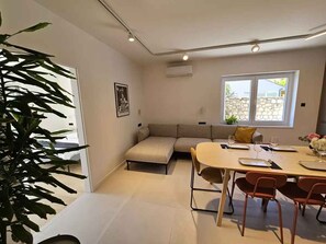 Een moderne woonruimte met een bank, eettafel, stoelen en een grote plant.
