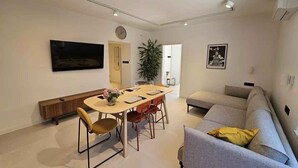 A modern living room with a sofa, a dining table with chairs, a TV mounted on the wall, and a plant. - Holiday apartment with air conditioning (Crikvenica)