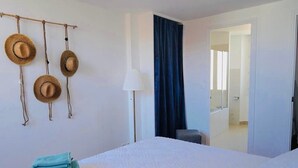 Hotellihuone, jossa on sänky, lamppu, tuoli ja ovi, joka johtaa kylpyhuoneeseen.