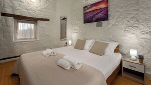 A bedroom with a large bed, a nightstand, a bedside table, a window with curtains, a wall-mounted mirror, and a painting of a field. - Finca with pool and garden, pets welcome (Vižinada)