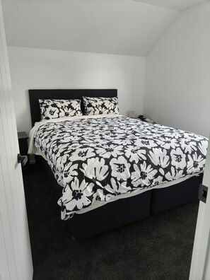 A bedroom with a bed, two pillows, a nightstand, and a door. - 2-bedroom apartment in marvelous Christchurch with AC and comfort (Christchurch)