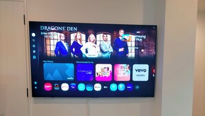En platt-TV som är monterad på en vägg och visar ett användargränssnitt för en streamingtjänst med olika innehållsalternativ.