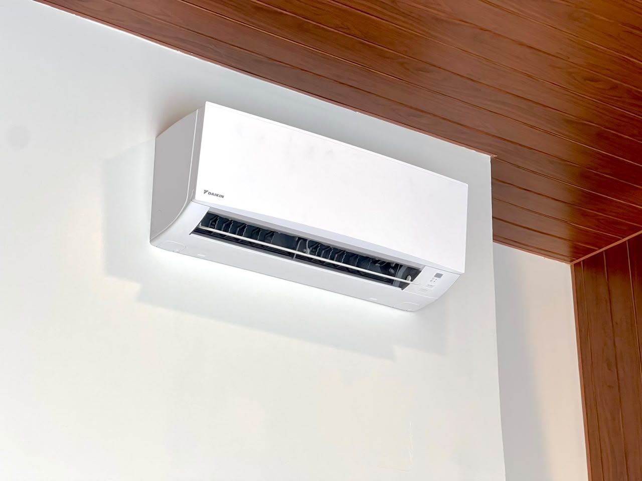 A white air conditioning unit mounted on a wall with a wooden ceiling.