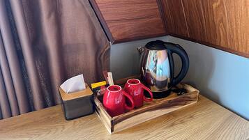 A wooden tray with a tissue box, a red mug, and a stainless steel kettle on a wooden table.
