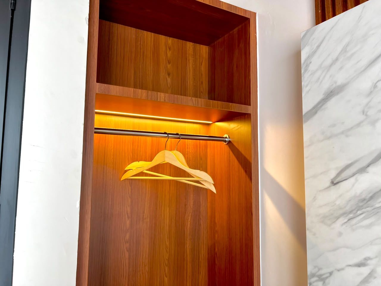 Ein Holfschrank mit Kleiderstange neben einer Marmorwand.