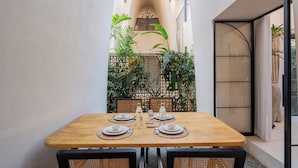 A dining table set with plates, glasses, and cutlery, surrounded by wicker chairs, with a view of a garden and a building in the background. - ELIVAAS Bogenvilla Luxe 3 BHK Villa (Anjuna)