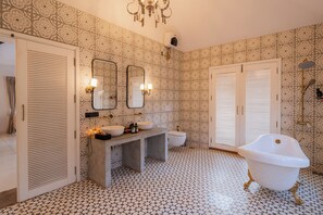 A bathroom with patterned wallpaper, a freestanding bathtub, a vanity with a mirror, and a toilet. - ELIVAAS Bogenvilla Luxe 3 BHK Villa (Anjuna)