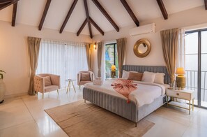 A bedroom with a large bed, two chairs, a bedside table with a lamp, and a window with curtains. - ELIVAAS Bogenvilla Luxe 3 BHK Villa (Anjuna)