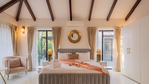 A bedroom with a large bed, a chair, a nightstand, an air conditioning unit, and a wardrobe. - ELIVAAS Bogenvilla Luxe 3 BHK Villa (Anjuna)