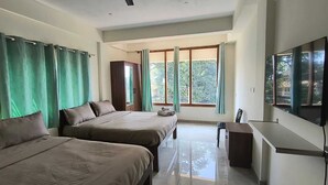 A hotel room with two beds, a desk, a TV, and a large window with curtains. - Ameya Coorg (Madikeri)