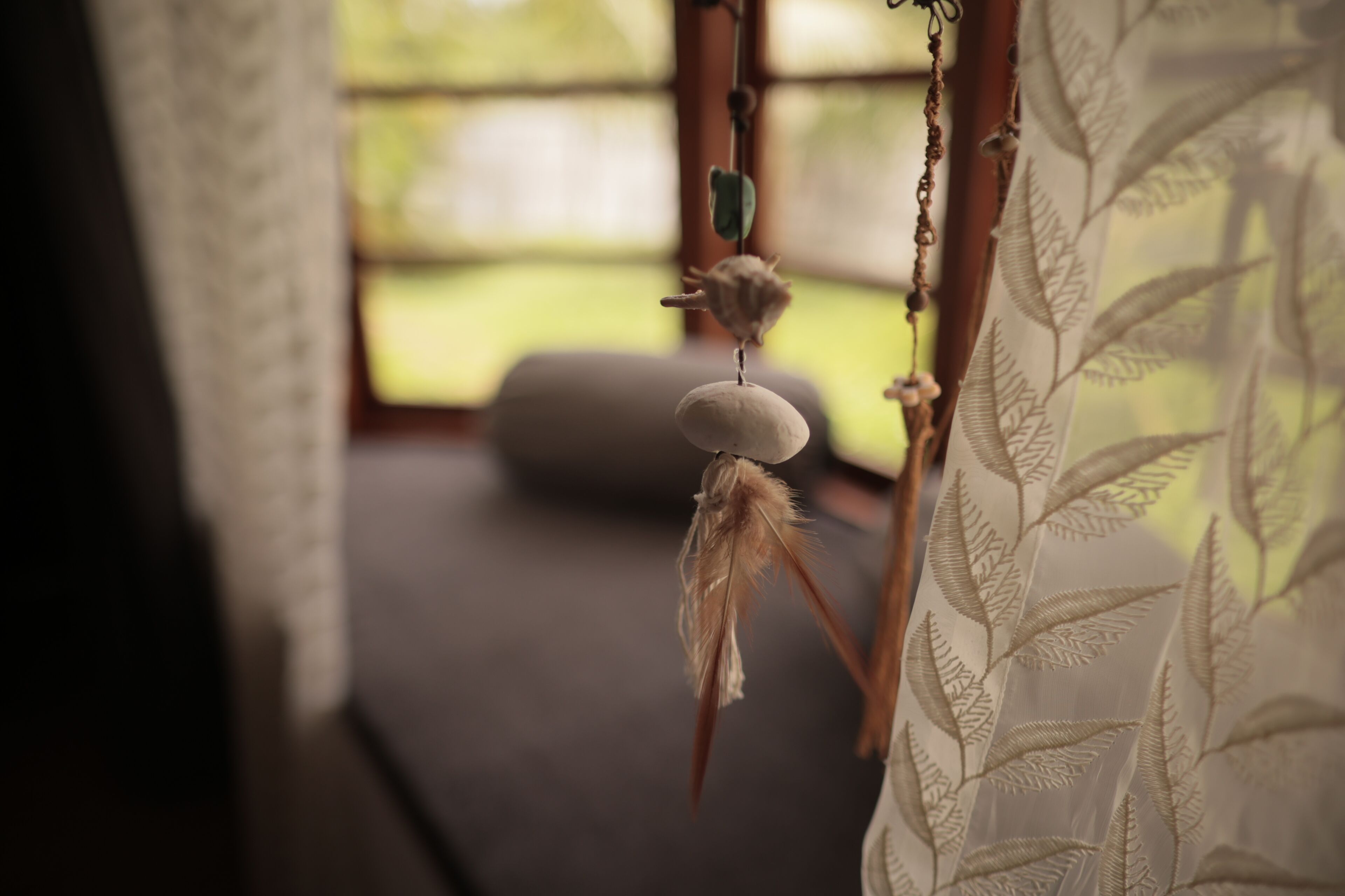 A room with a hanging ornament, a cushion, and a window with a view of greenery.