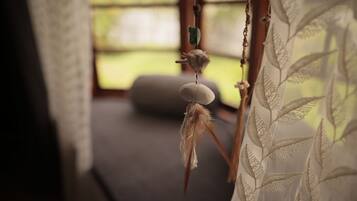 A room with a hanging ornament, a cushion, and a window with a view of greenery.