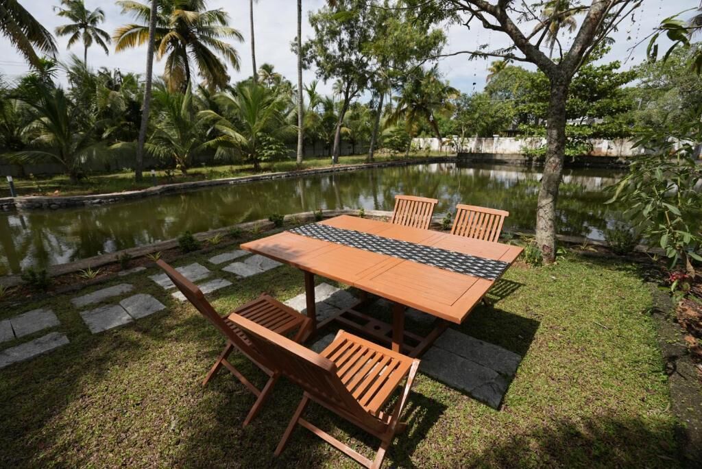 A wooden table and chairs set on a lawn with a pond and palm trees in the background.