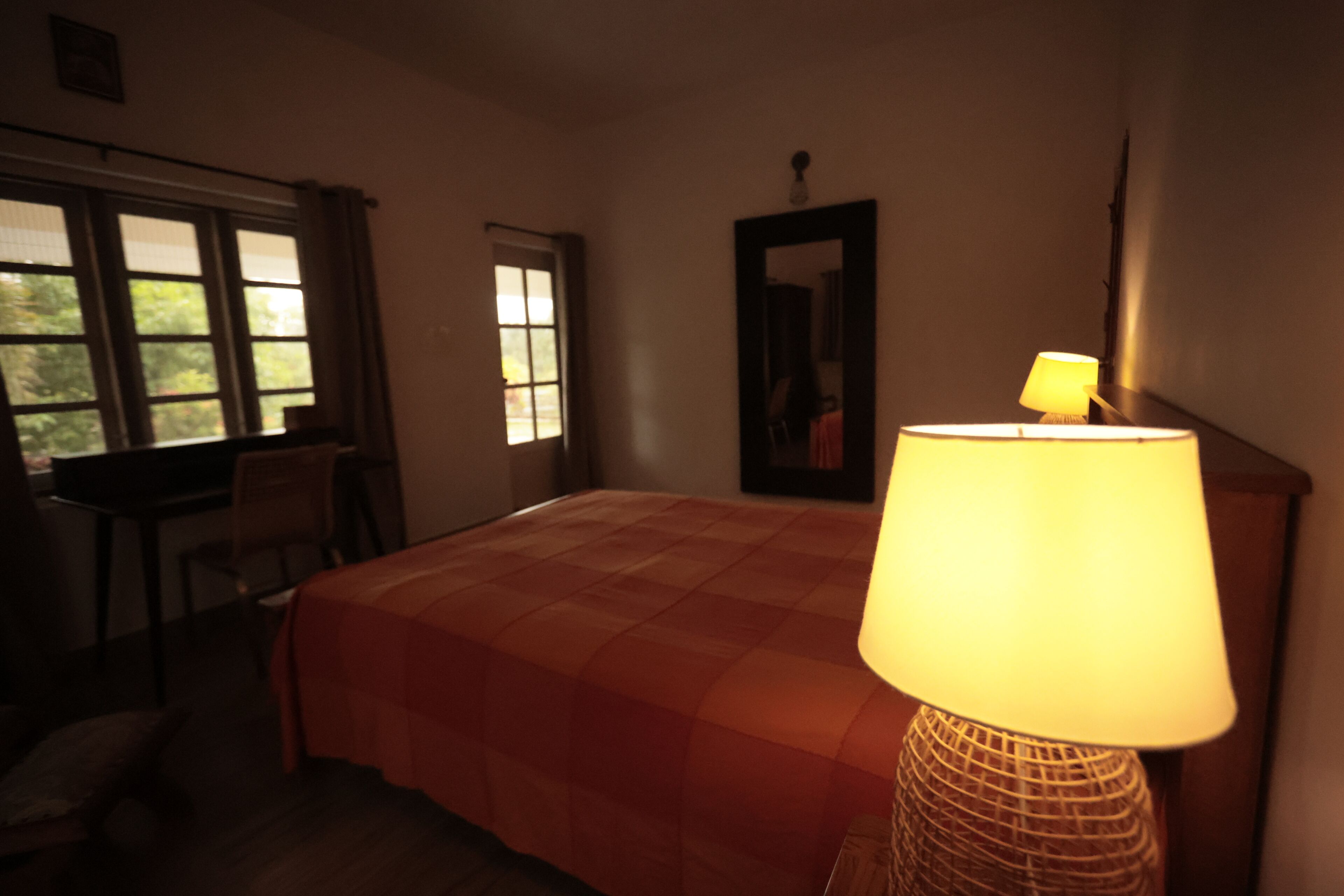 A hotel room with a bed, a desk, a chair, a lamp, and a window.