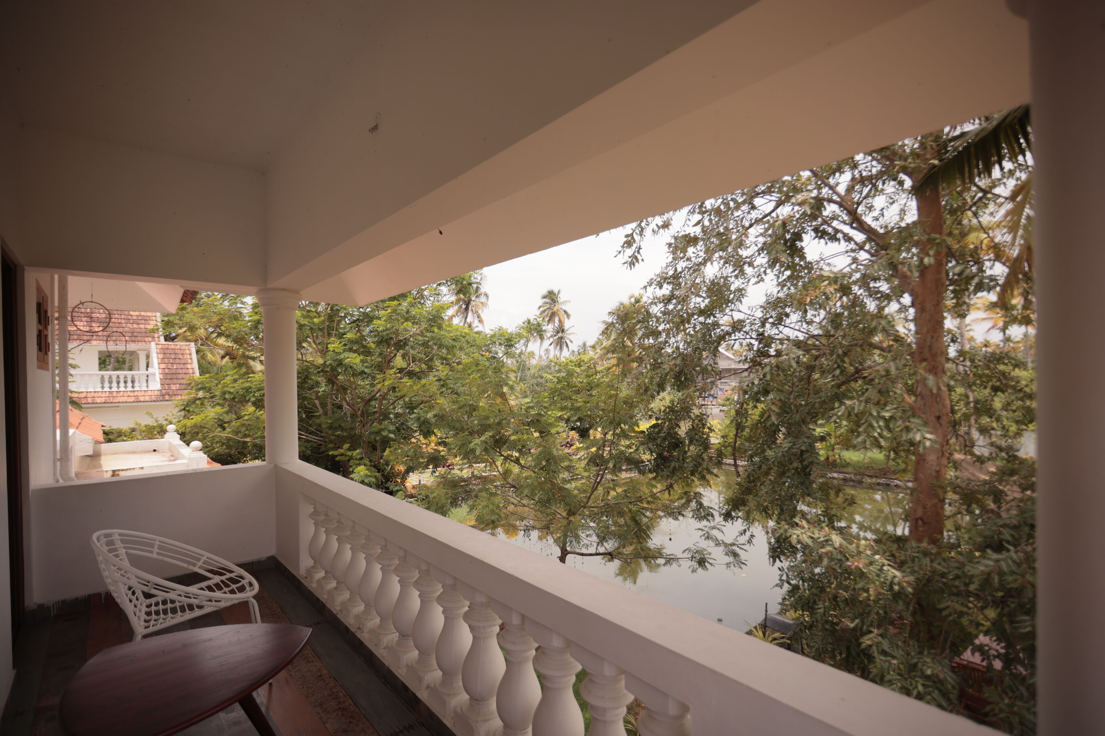 A balcony with a white balustrade, a wooden chair, and a view of a pond surrounded by trees.