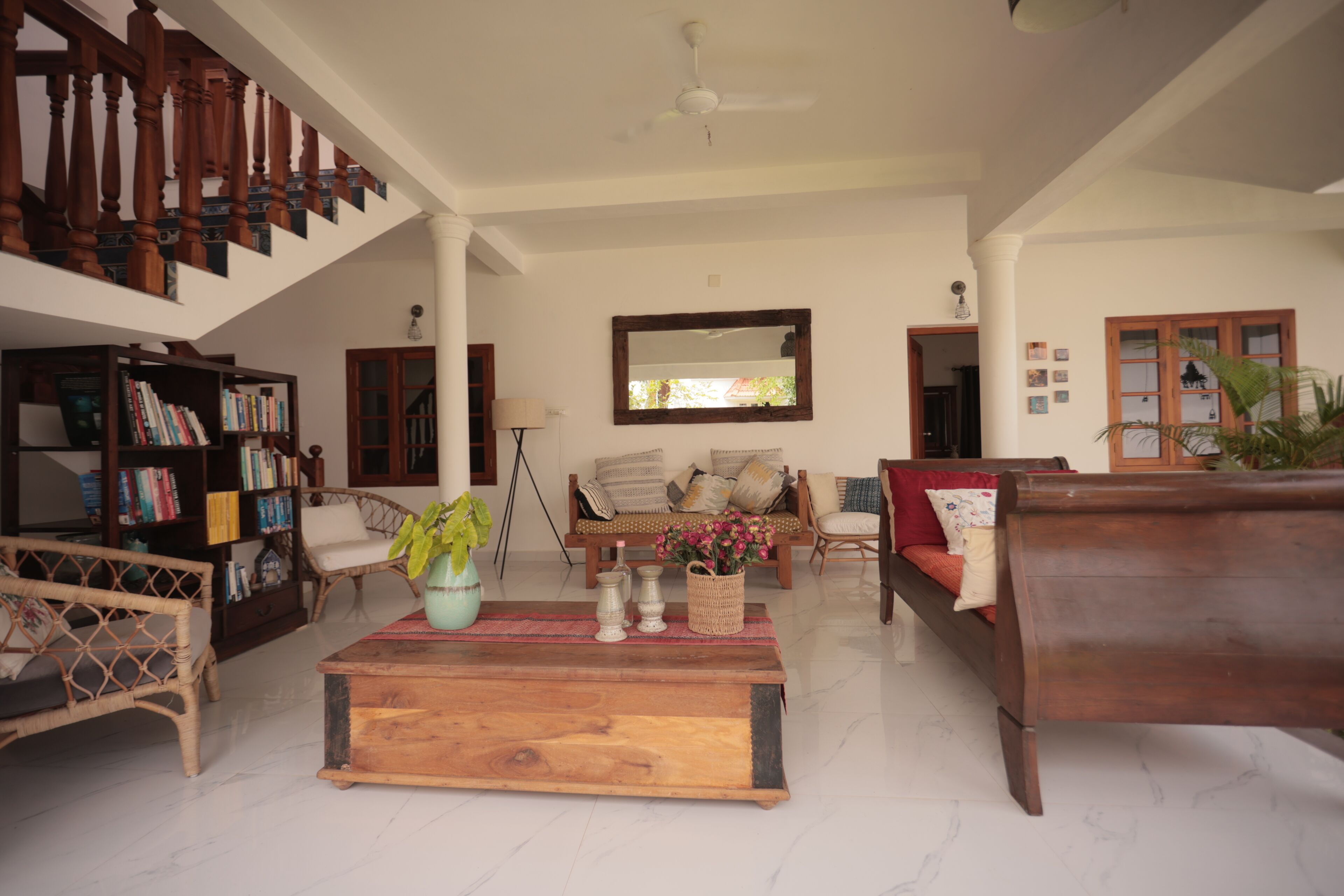 A spacious living room with a high ceiling, a wooden staircase, a large mirror, and a variety of seating options including a sofa and chairs.