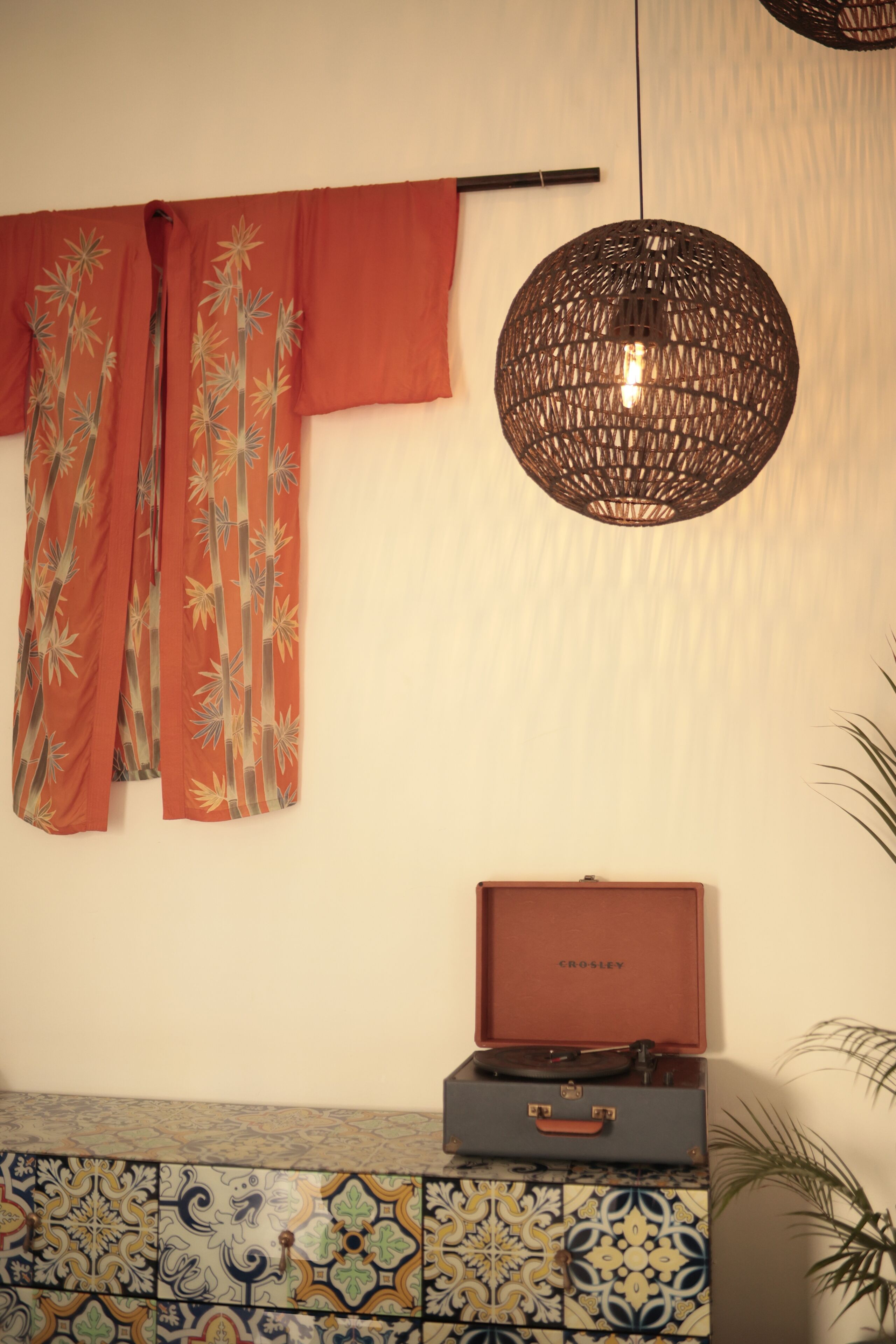 A room with a patterned wall, a hanging lamp, a vintage suitcase, and a plant.