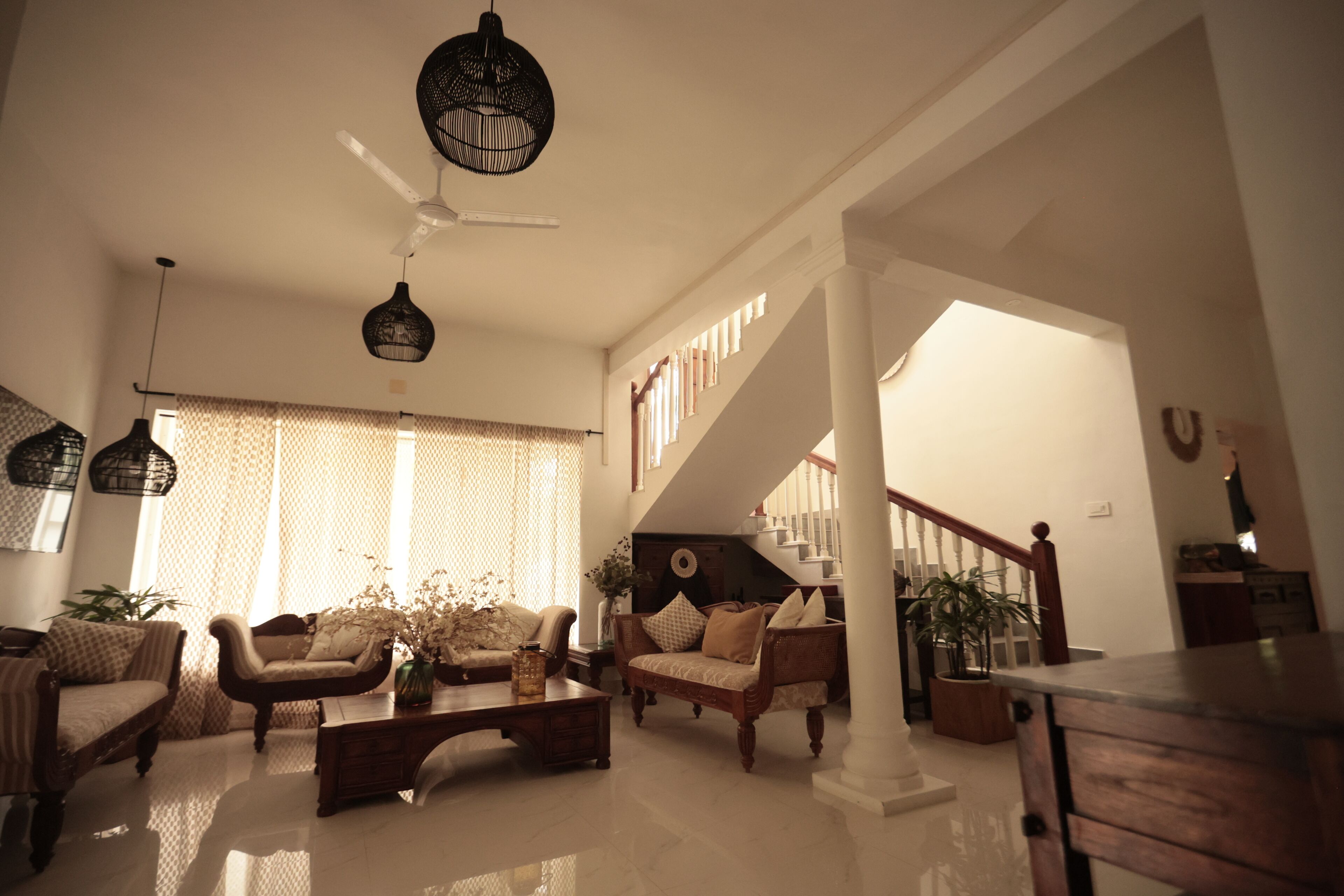 A spacious living room with a high ceiling, a staircase, and a large window with curtains.