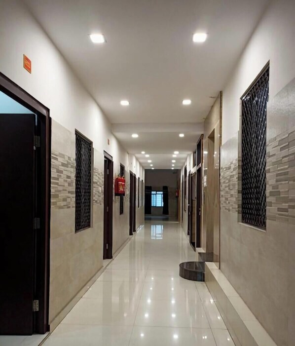 A hotel hallway with doors on both sides, a tiled floor, and recessed lighting. - Chhabra Hotel Kanpur (Kanpur)
