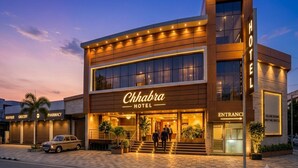 Ein Hotel mit moderner Fassade, einem gut sichtbaren Eingang und Hinweisen auf ein Boutique-Geschäft, einen Supermarkt und eine Apotheke.