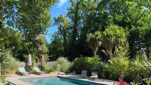 Una piscina rectangular con cubierta de madera, rodeada de abundante follaje y árboles.