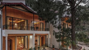 A two-story wooden building with balconies, large windows, and a landscaped garden with pathways and potted plants. - ELIVAAS 1BHK Pine View Resort  (Krishangarh)