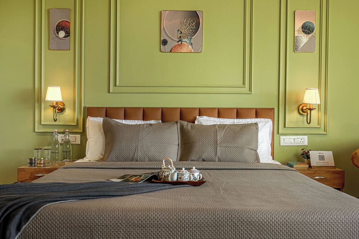 A neatly arranged hotel room with a bed, bedside lamps, a tray with tea and cups, and wall art.