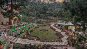 A landscaped garden with pathways, a central lawn, and surrounding trees. - ELIVAAS 1BHK Pine View Resort  (Krishangarh)