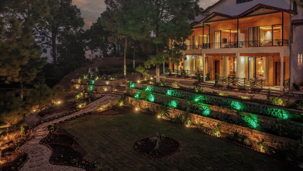 A two-story building with a balcony, surrounded by trees and illuminated pathways. - ELIVAAS 1BHK Pine View Resort  (Krishangarh)