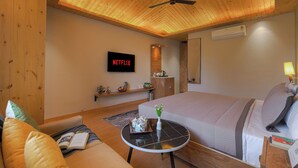 A cozy hotel room with a large bed, a television displaying 'NETFLIX,' a wooden ceiling, and a small table with a vase. - ELIVAAS 1BHK Pine View Resort  (Krishangarh)