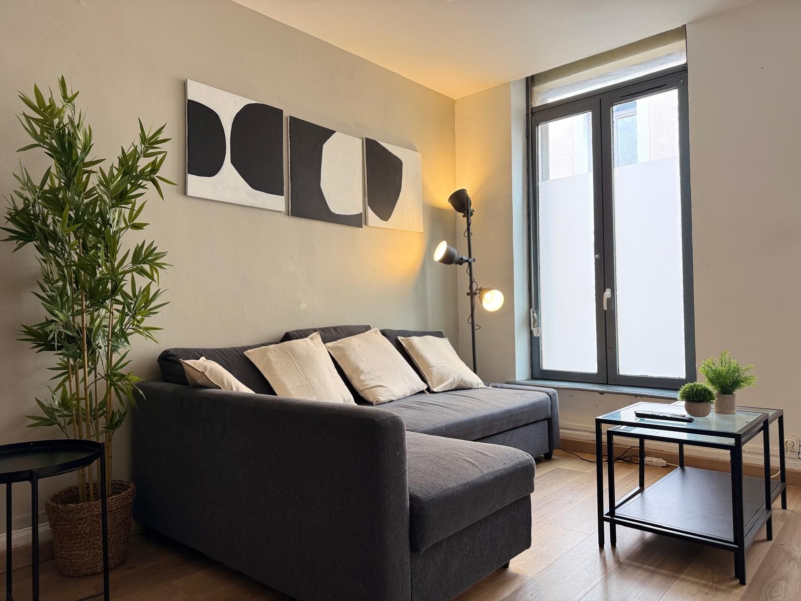 Un salon moderne avec un canapé, une lampe sur pied, une petite table et une grande fenêtre.