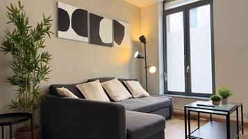 Un salon moderne avec un canapé, une lampe sur pied, une petite table et une grande fenêtre.