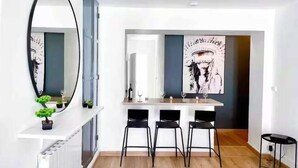 A modern kitchen with a dining area, featuring a white countertop, black chairs, and a large mirror.