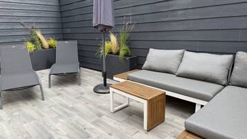 A modern outdoor seating area with a grey sofa, two chairs, a wooden table, and a potted plant.