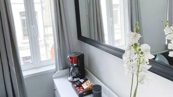 A hotel room with a large mirror, a coffee maker, a small plant, and a window with curtains.