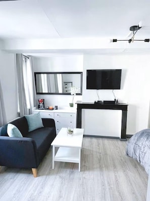 A modern hotel room with a sofa, a small table, a TV, a desk, and a bed. - The Refuge of the Squares (Arras)
