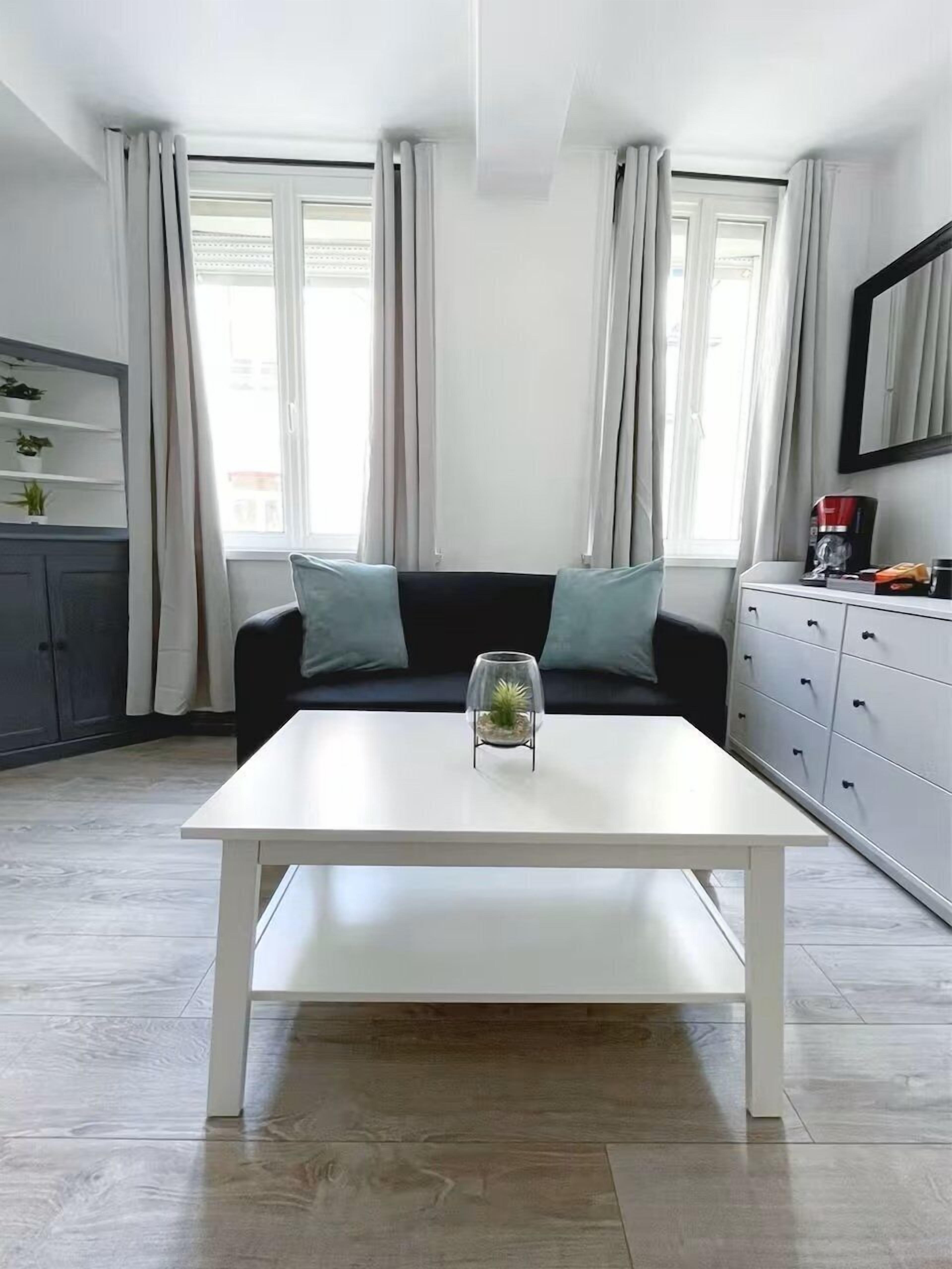 Una sala de estar moderna con una mesa blanca, un sofá negro y una planta pequeña sobre la mesa.